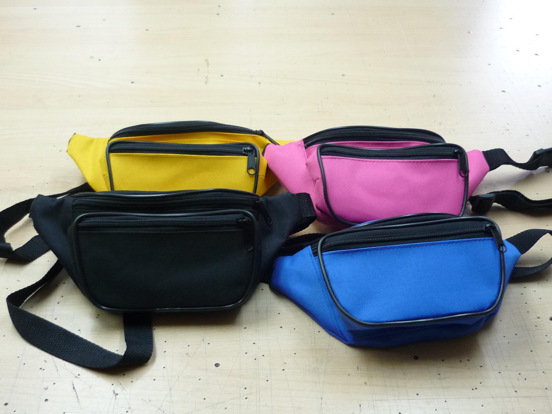 Cztery saszetki biodrowe w kolorach żółtym, różowym, czarnym i niebieskim leżą na drewnianym blacie.