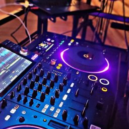 MAGDALENA BARSZCZ - DJ w Otwocku miksuje muzykę na profesjonalnym sprzęcie, widoczny laptop z oprogramowaniem DJ-skim i podświetlane elementy konsoli.