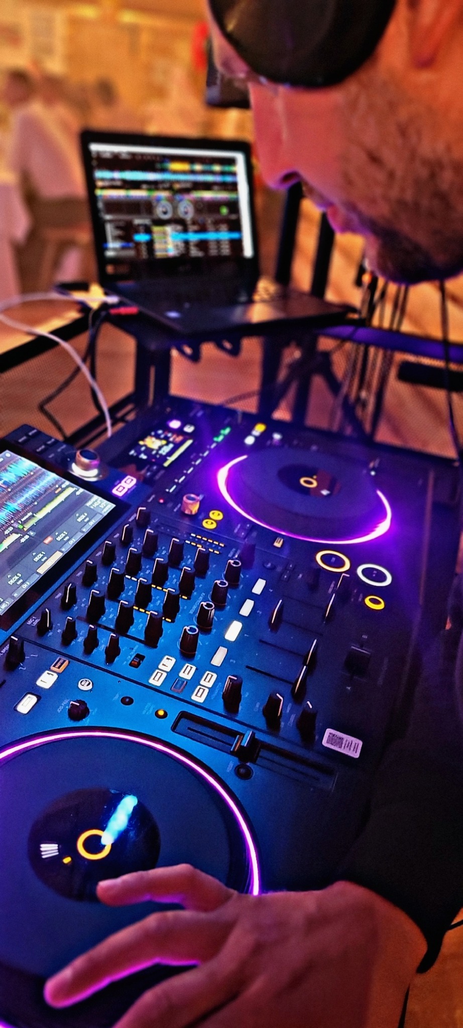 DJ w Otwocku miksuje muzykę na profesjonalnym sprzęcie, widoczny laptop z oprogramowaniem DJ-skim i podświetlane elementy konsoli.
