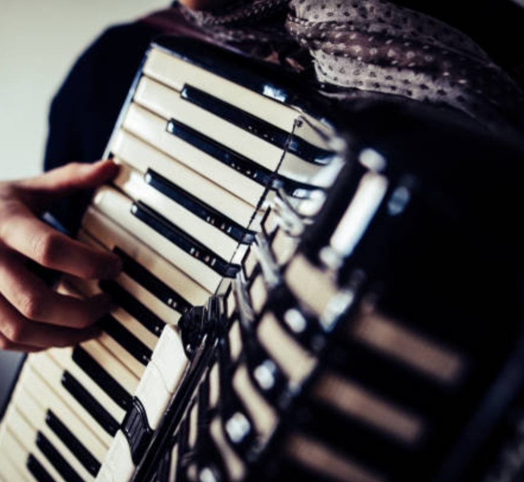 Akordeon w rękach muzyka, widoczny fragment wzorzystej apaszki na szyi, ujęcie z bliska na klawisze i miech instrumentu.