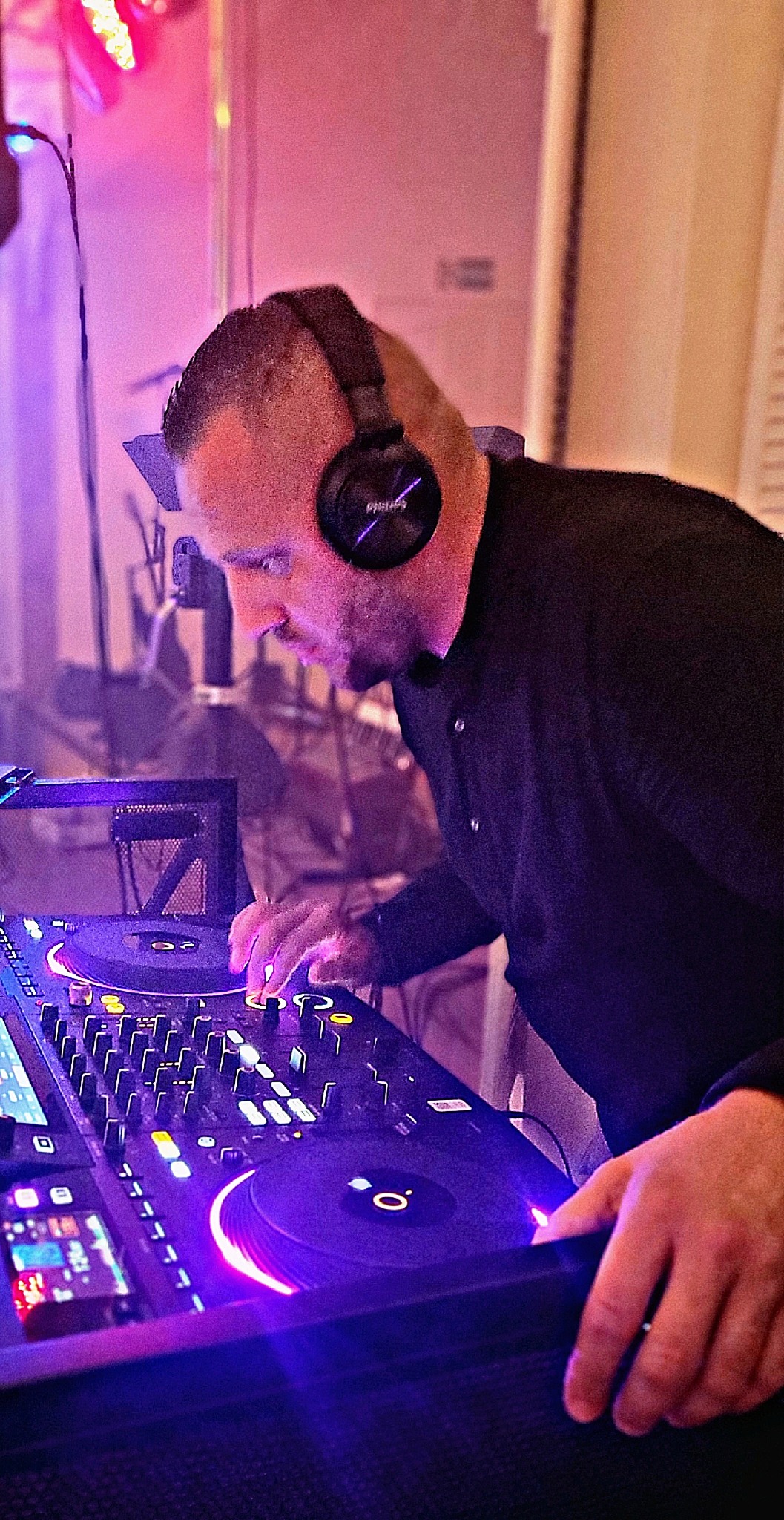 DJ w słuchawkach, miksujący muzykę na profesjonalnym sprzęcie w fioletowo-różowym oświetleniu, skupiony na pracy.
