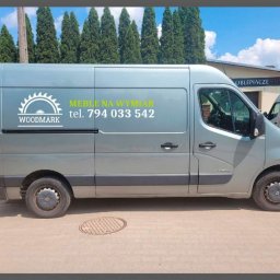 Woodmark - Szary samochód dostawczy z logo firmy Woodmark i napisem 'Meble na wymiar' oraz numerem telefonu, zaparkowany na ulicy w słoneczny dzień.