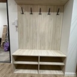 Woodmark - Jasna zabudowa przedpokoju z wieszakami i półkami na buty, wykonana z płyty imitującej drewno. Minimalistyczny design, widoczne elementy wykończenia wnętrza.