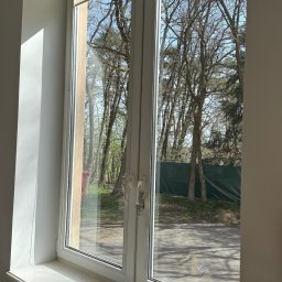 MM Cleaning Mykhailo Mykhalchuk - Białe okno z roletami, widok na drzewa i chodnik na zewnątrz. Widoczne ślady użytkowania na parapecie.