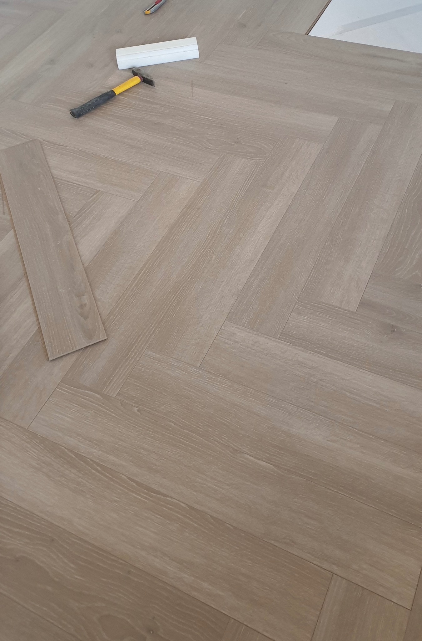 Układanie paneli podłogowych w jodełkę w Szczecinie, widoczny młotek i listwa przypodłogowa, fragment niedokończonej podłogi.