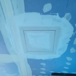 DaJF MAKSYMILIAN BOREK - Niebieska płyta karton-gips z zamontowaną klapą rewizyjną, otoczona świeżo nałożoną gładzią szpachlową, widoczne ślady po wkrętach i łączeniach płyt.