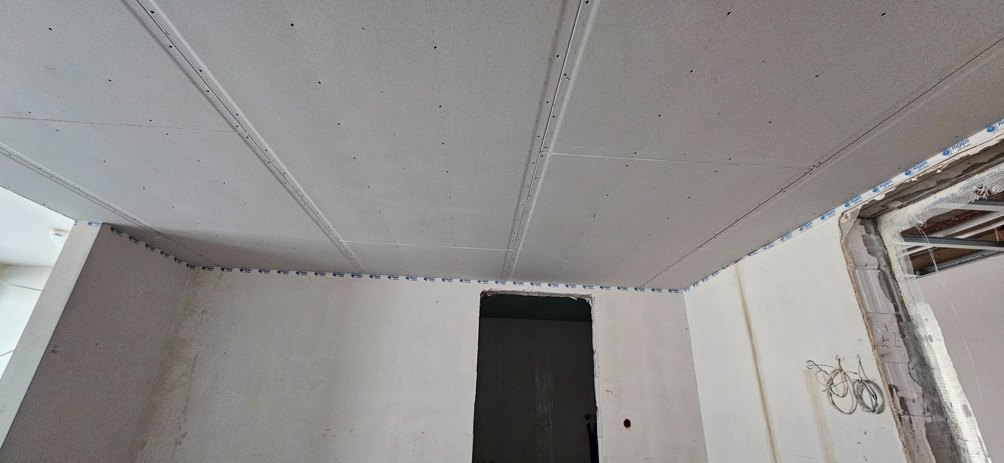 Sufit z płyt kartonowo-gipsowych w trakcie montażu, widoczne profile i taśma Rigips na styku ścian, surowy stan wykończenia.