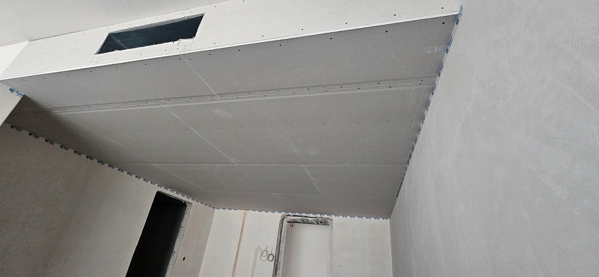 Montaż sufitu podwieszanego z płyty gipsowo-kartonowej z otworem rewizyjnym, widoczne profile i mocowania.