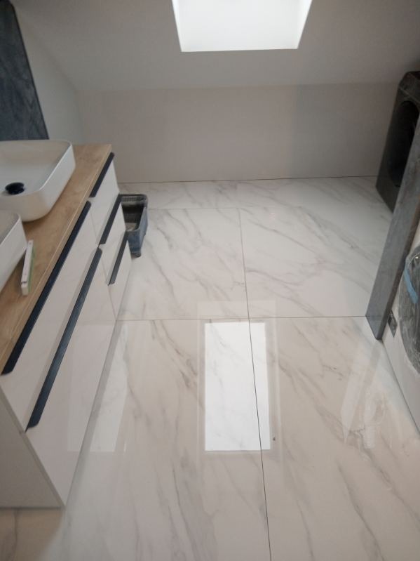 Wykończona łazienka na poddaszu z marmurowymi płytkami podłogowymi, białą szafką z umywalkami i oknem dachowym.