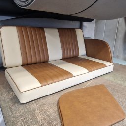 Usługi Tapicerskie Sebastian Kasperski - Kanapa z brązowo-kremową tapicerką w paski, obok leży poduszka, nad nią rolka materiału tapicerskiego