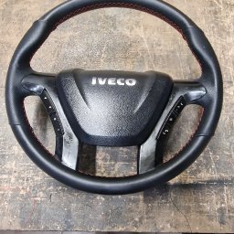 Usługi Tapicerskie Sebastian Kasperski - Odnowiona kierownica Iveco z czarną skórą i czerwonym szwem, leżąca na warsztatowym stole, obok opalarki.