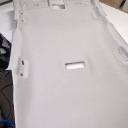 Usługi Tapicerskie Sebastian Kasperski - Jasnoszara podsufitka samochodowa z wycięciami na oświetlenie i mocowania, leżąca na stole w warsztacie.