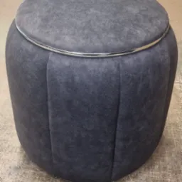 Szary puf tapicerowany welurem z metalową obręczą, widoczne pionowe przeszycia.