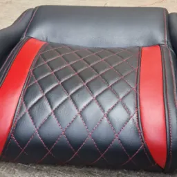 Czarne samochodowe siedzenie z czerwonymi wstawkami, pikowane w romby i obszyte czerwoną nicią, leżące na szarym podłożu.