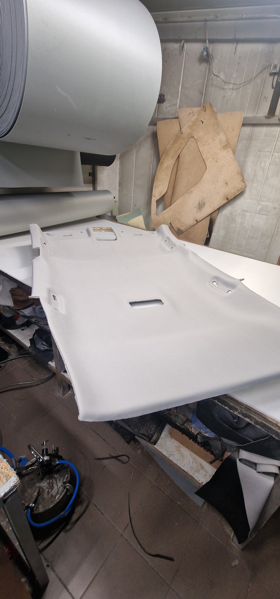 Szary podsufitka samochodowa na stole warsztatowym, obok rolka materiału i szablony z tektury.