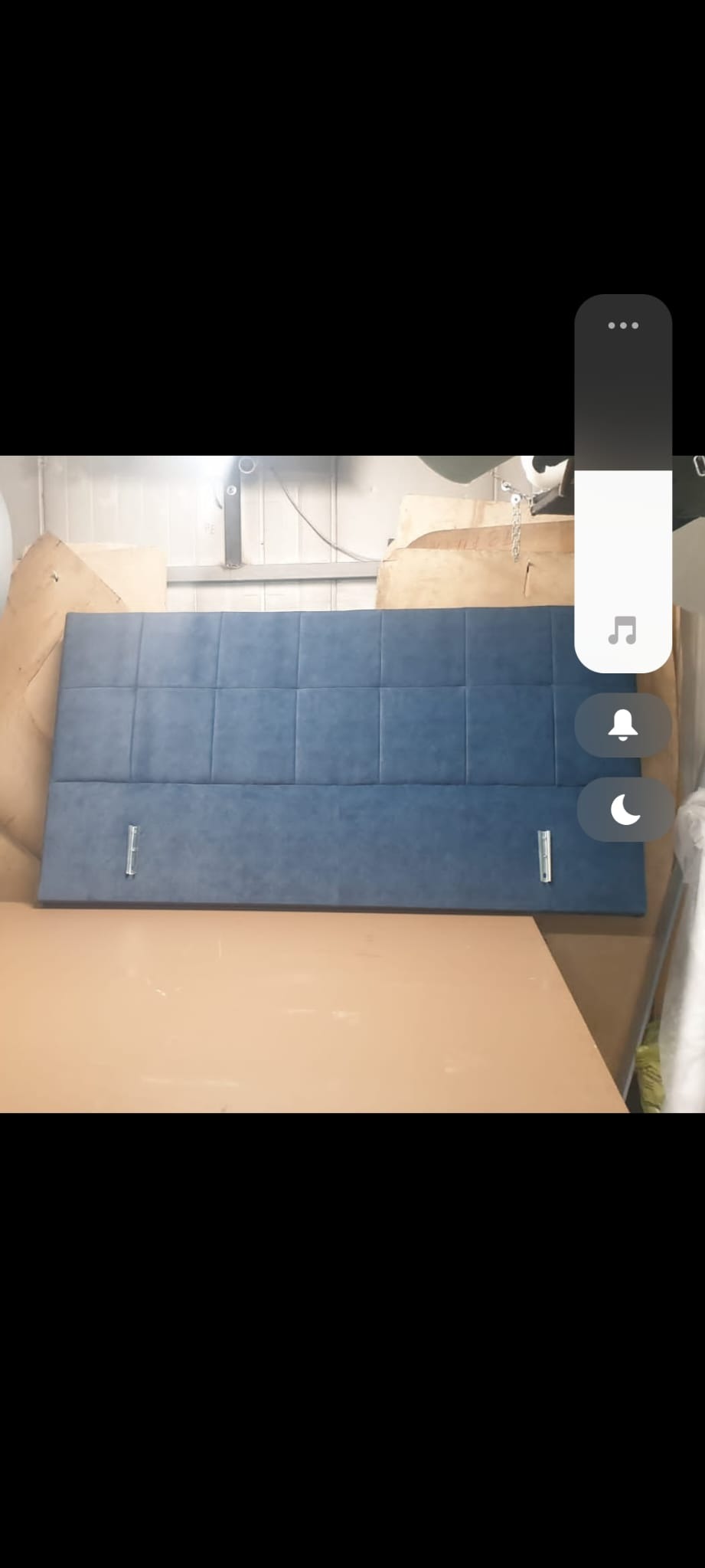 Tapicerowany zagłówek do łóżka w odcieniach niebieskiego, z kwadratowymi przeszyciami, przymocowany do drewnianej ramy za pomocą metalowych uchwytów.