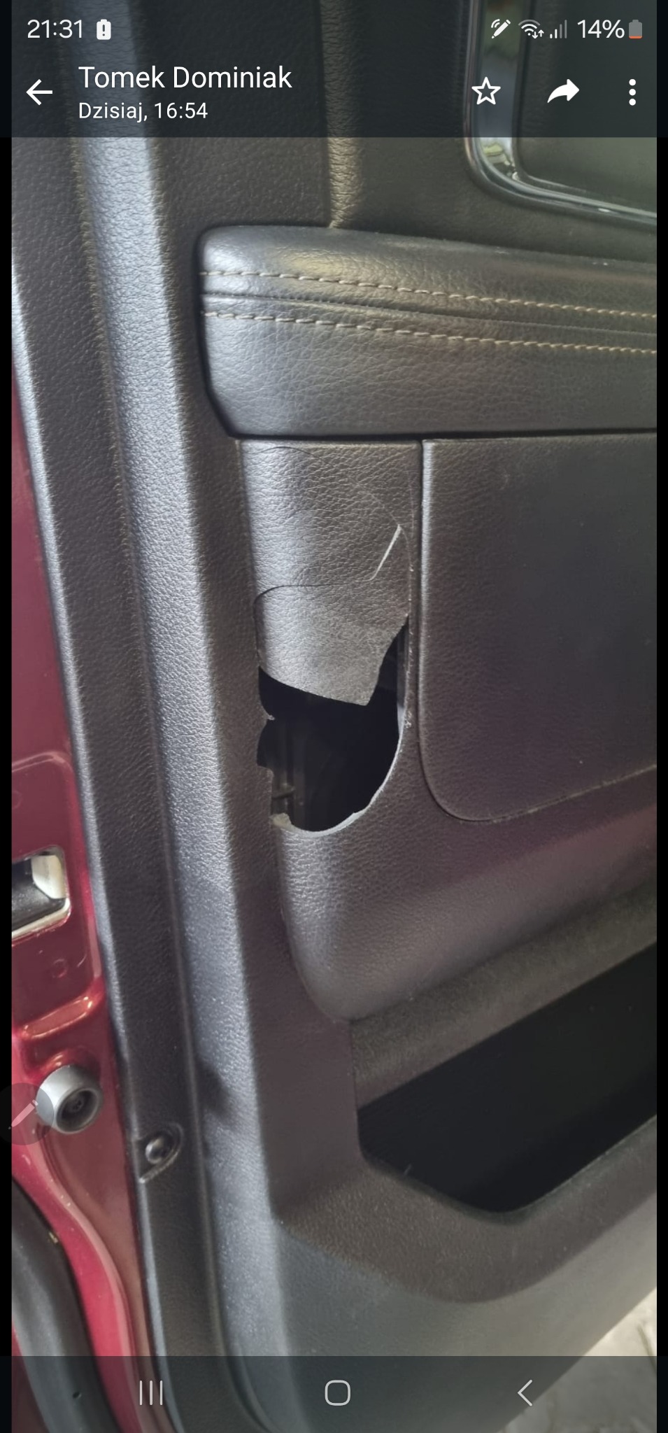 Uszkodzony, czarny panel tapicerowany drzwi samochodu z widocznym pęknięciem i ubytkiem materiału.