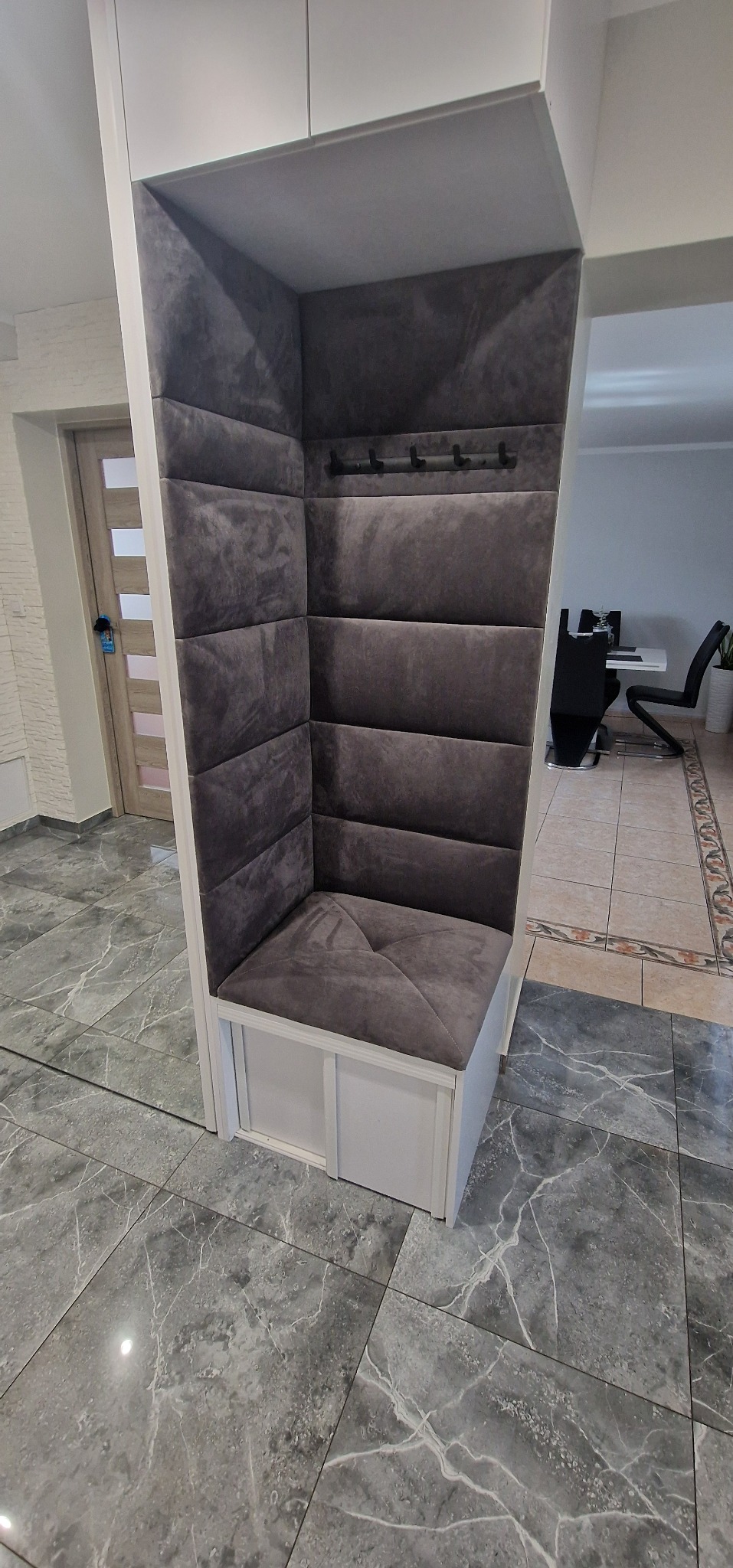 Szary, tapicerowany narożnik z wieszakami w przedpokoju, widok z boku, marmurowa podłoga.