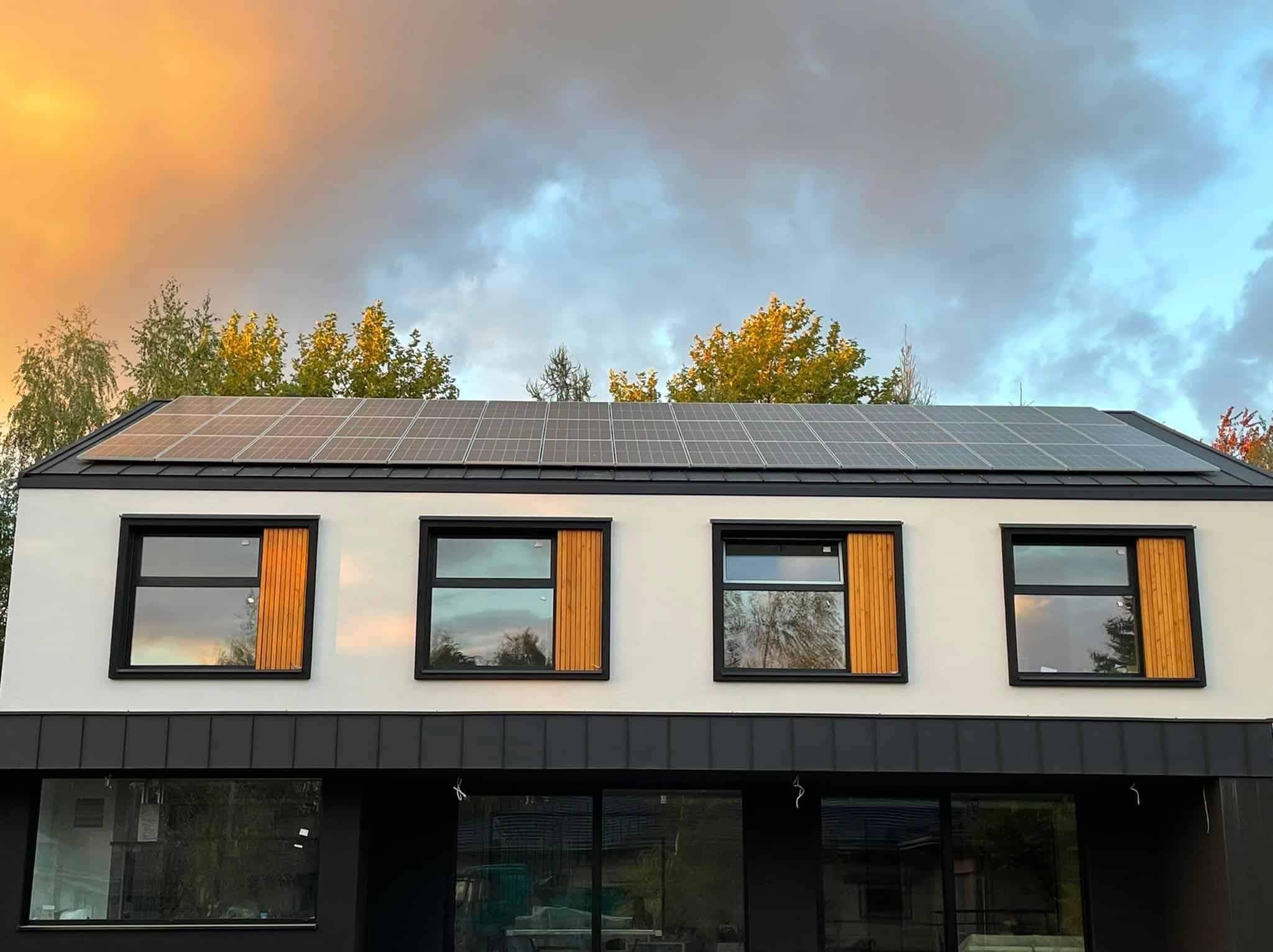 Nowoczesny dom z panelami słonecznymi na dachu w świetle zachodzącego słońca, widoczne drewniane okiennice.