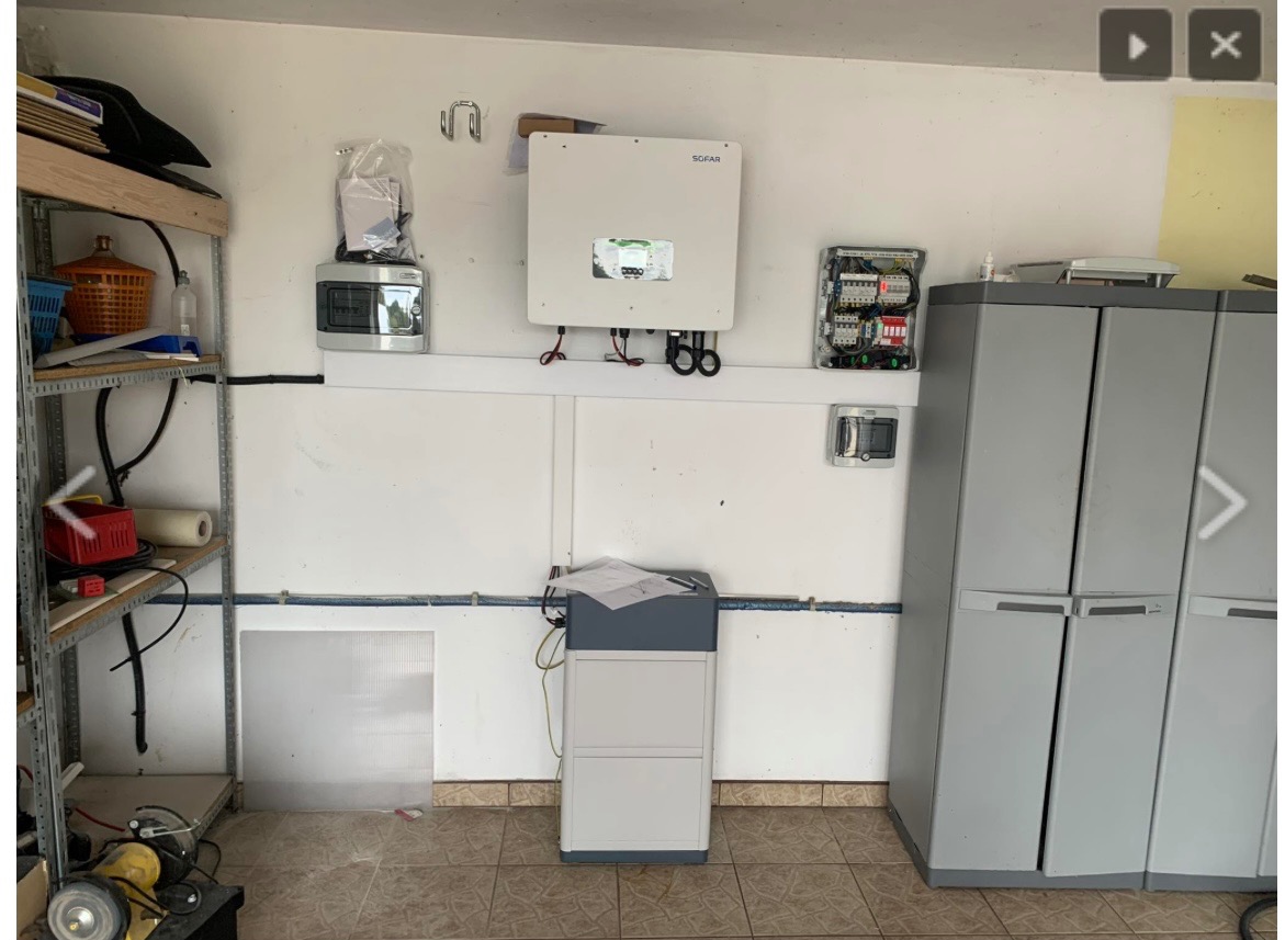 Wnętrze garażu z zamontowanym inwerterem firmy Sofar, rozdzielnicą elektryczną, magazynem energii na podłodze oraz metalowym regałem z narzędziami i akcesoriami.