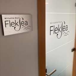 PM SSC SPÓŁKA Z OGRANICZONĄ ODPOWIEDZIALNOŚCIĄ - Tabliczka z napisem 'Wirtualne Biuro Fleksea' na ścianie obok szklanych drzwi z tym samym napisem, widok z bliska.