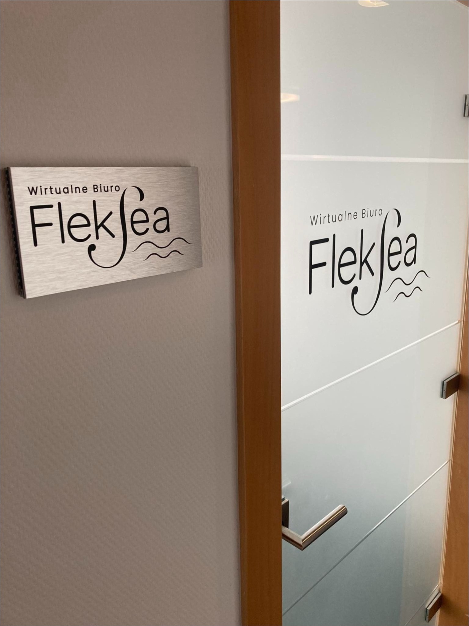 Tabliczka z napisem 'Wirtualne Biuro Fleksea' na ścianie obok szklanych drzwi z tym samym napisem, widok z bliska.