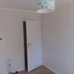 Met -Bud - Wnętrze pokoju po odmalowaniu ścian na biało, widoczna biała ościeżnica z otwartymi drzwiami, drewniana podłoga oraz lampa sufitowa z motywem pociągów i samolotów.