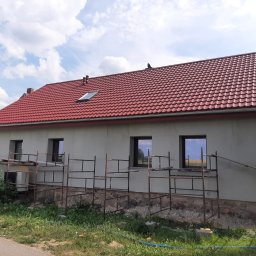 Met -Bud - Dom jednorodzinny w trakcie prac wykończeniowych elewacji, widoczne rusztowania, ściany otynkowane na szaro, czerwony dach z dachówki, okna z ciemnymi ramami.