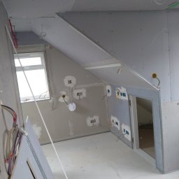 Met -Bud - Wnętrze poddasza w trakcie prac wykończeniowych: zamontowane płyty gipsowo-kartonowe na ścianach i skosach, widoczne instalacje elektryczne, przygotowane otwory na gniazdka, surowe wykończenie...