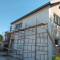 Met -Bud - Budynek jednorodzinny z białymi ścianami w trakcie ocieplania, widoczne rusztowania i deski, fragment elewacji jeszcze nieocieplony.