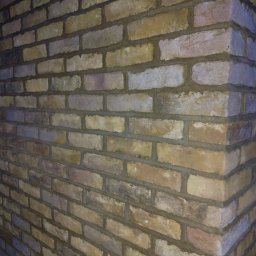 Met -Bud - Fragment narożnej ściany z cegły klinkierowej w odcieniach beżu, brązu i szarości, z widocznymi spoinami, oświetlonej z dwóch stron, tworzącej efekt cienia na jednej z płaszczyzn.