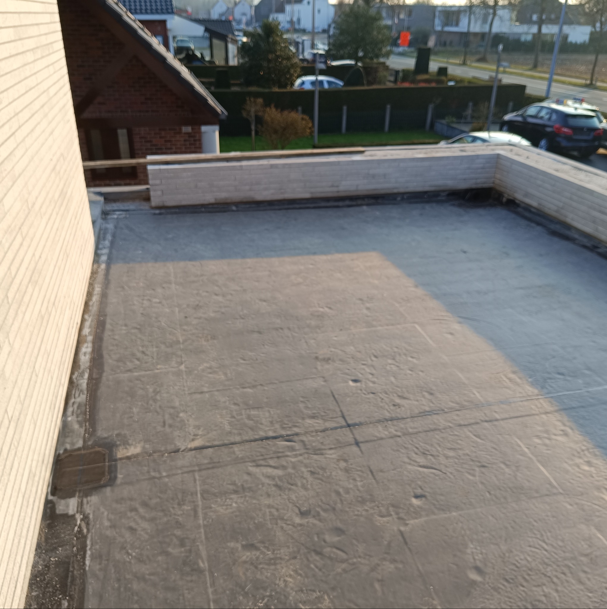 Płaski dach pokryty papą termozgrzewalną z widocznymi łączeniami, obrzeża wykończone cegłą, w tle zabudowa jednorodzinna.