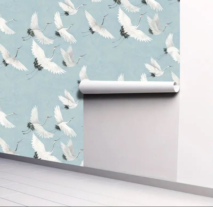 Ściana z częściowo nałożoną tapetą w delikatny wzór latających żurawi na błękitnym tle; reszta ściany biała, z częściowo rozwiniętą rolką tapety.
