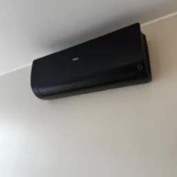 Czarny klimatyzator Haier zamontowany na jasnej ścianie. Widoczny z boku, z delikatnym oświetleniem, tworzy nowoczesny wygląd.