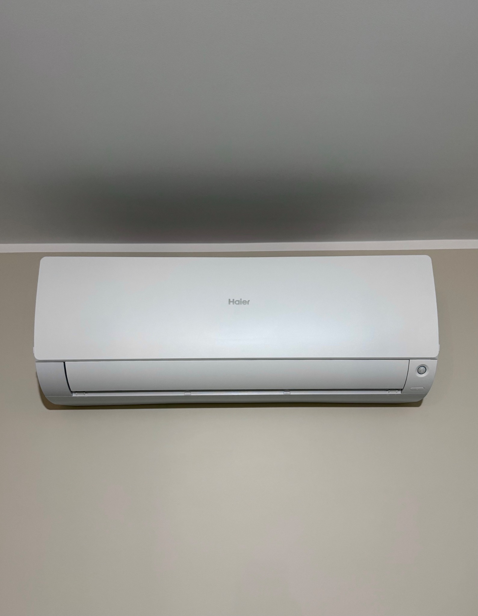 Biały klimatyzator Haier zamontowany na beżowej ścianie, widok z dołu.