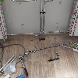 Hydro-Instal - Montaż instalacji centralnego ogrzewania z rur stalowych, widoczne narzędzia i elementy instalacji na podłodze z paneli.