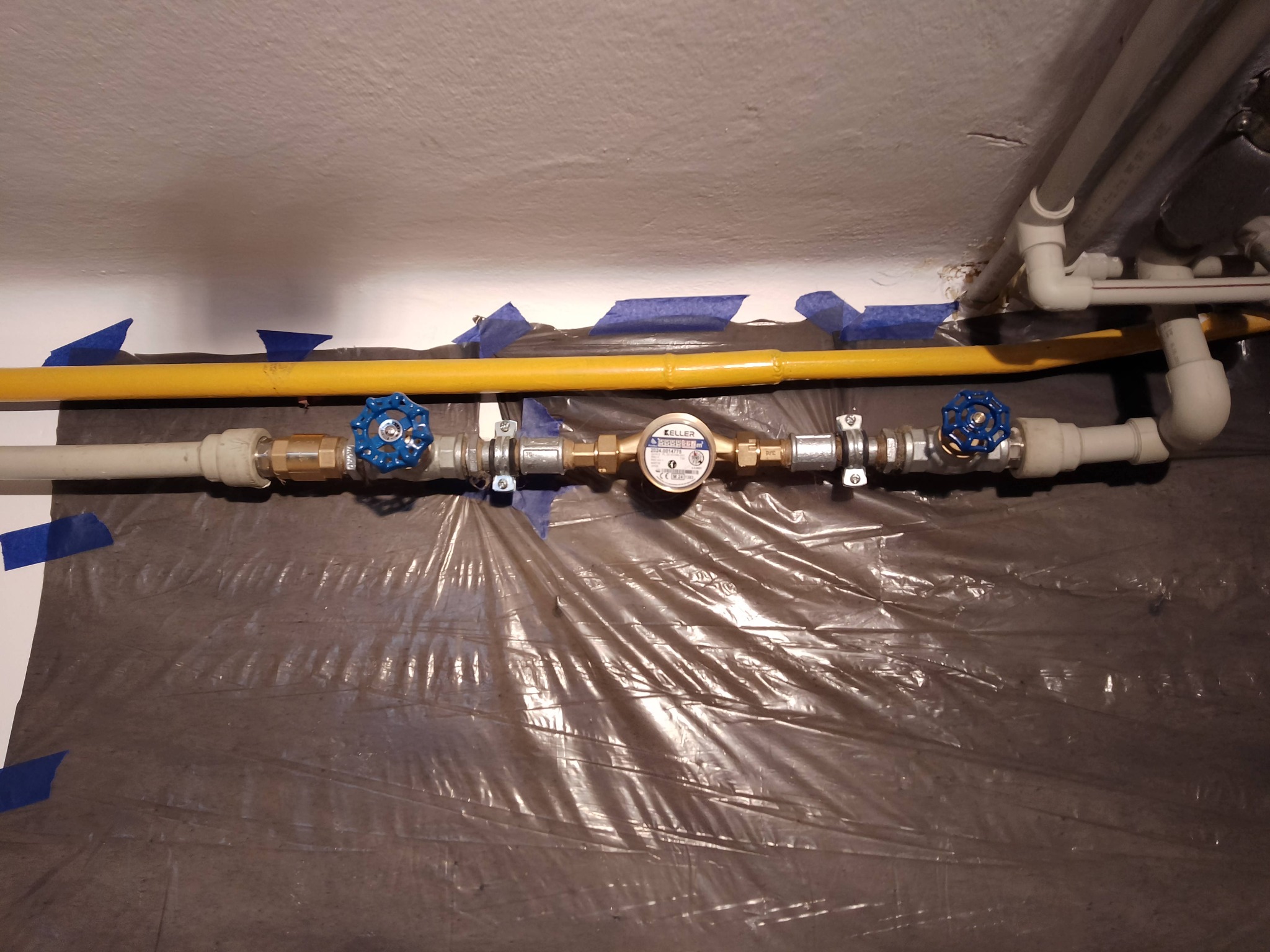 Szczegółowe ujęcie instalacji gazowej z licznikiem i zaworami, zabezpieczonej folią i taśmą malarską przed pracami remontowymi.