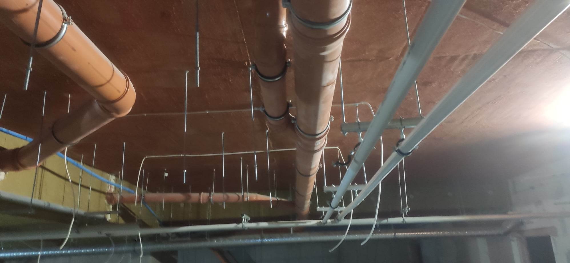 Widok instalacji kanalizacyjnej i wodnej pod stropem, z widocznymi rurami PCV, mocowaniami i elementami konstrukcyjnymi.