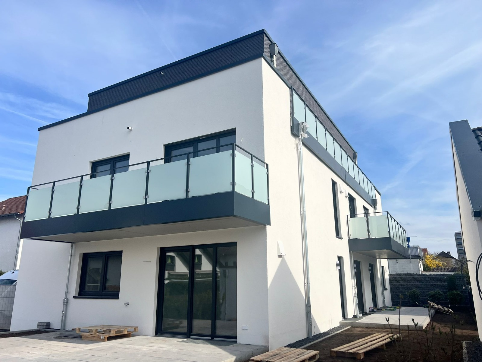 Nowoczesny budynek wielorodzinny z balkonami z balustradami ze szkła matowego i czarnymi ramami, widok z zewnątrz na tle błękitnego nieba.