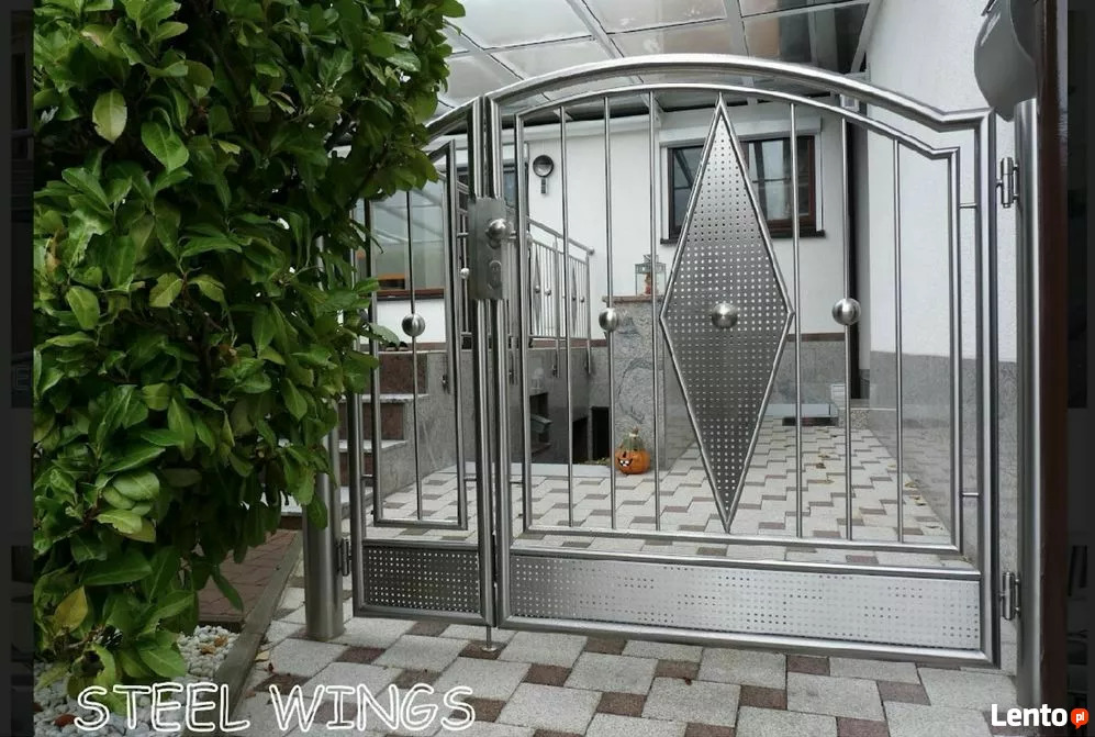 Nowoczesna, dwuskrzydłowa brama ze stali nierdzewnej z dekoracyjnym rombem i kulistymi elementami, widok z zewnątrz, z boku zielony krzew.