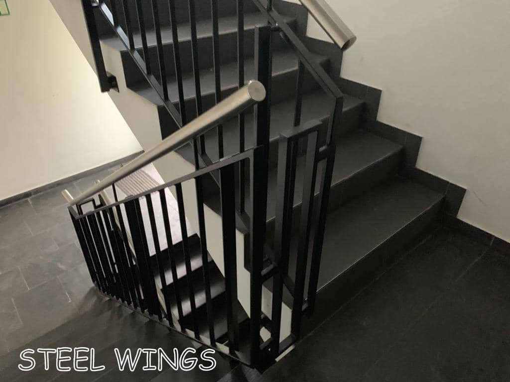 Wewnętrzne schody z czarnymi metalowymi balustradami z elementami ze stali nierdzewnej, widok z góry, ciemna podłoga z płytek.