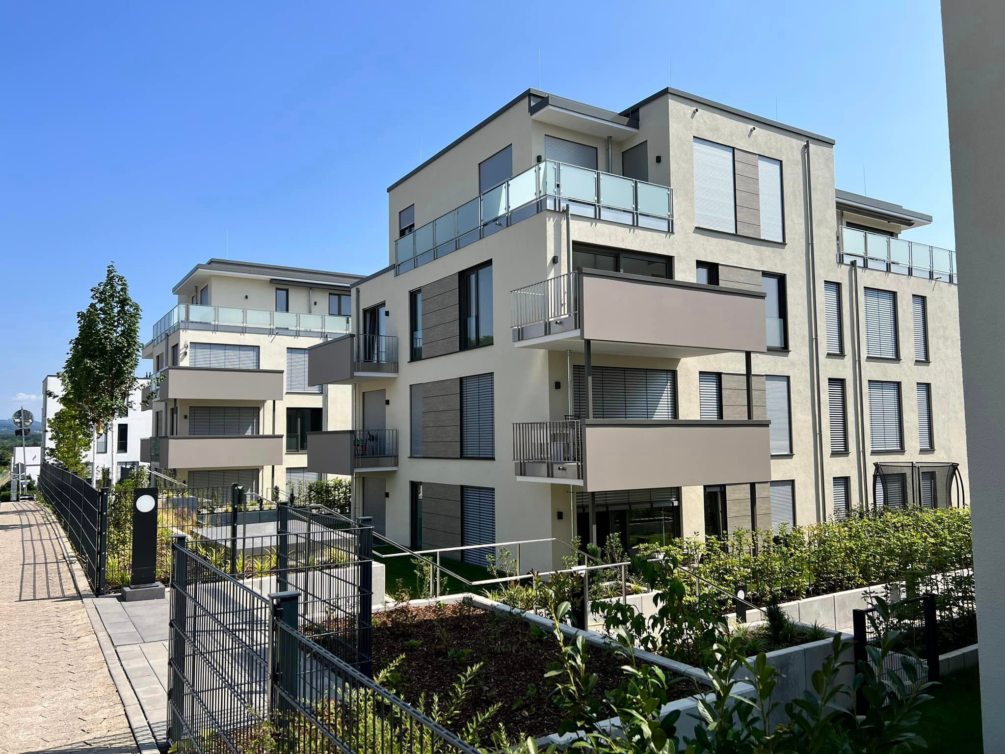 Nowoczesne budynki wielorodzinne z balkonami z balustradami ze szkła i metalu, ogrodzone panelowym ogrodzeniem w kolorze antracytowym.