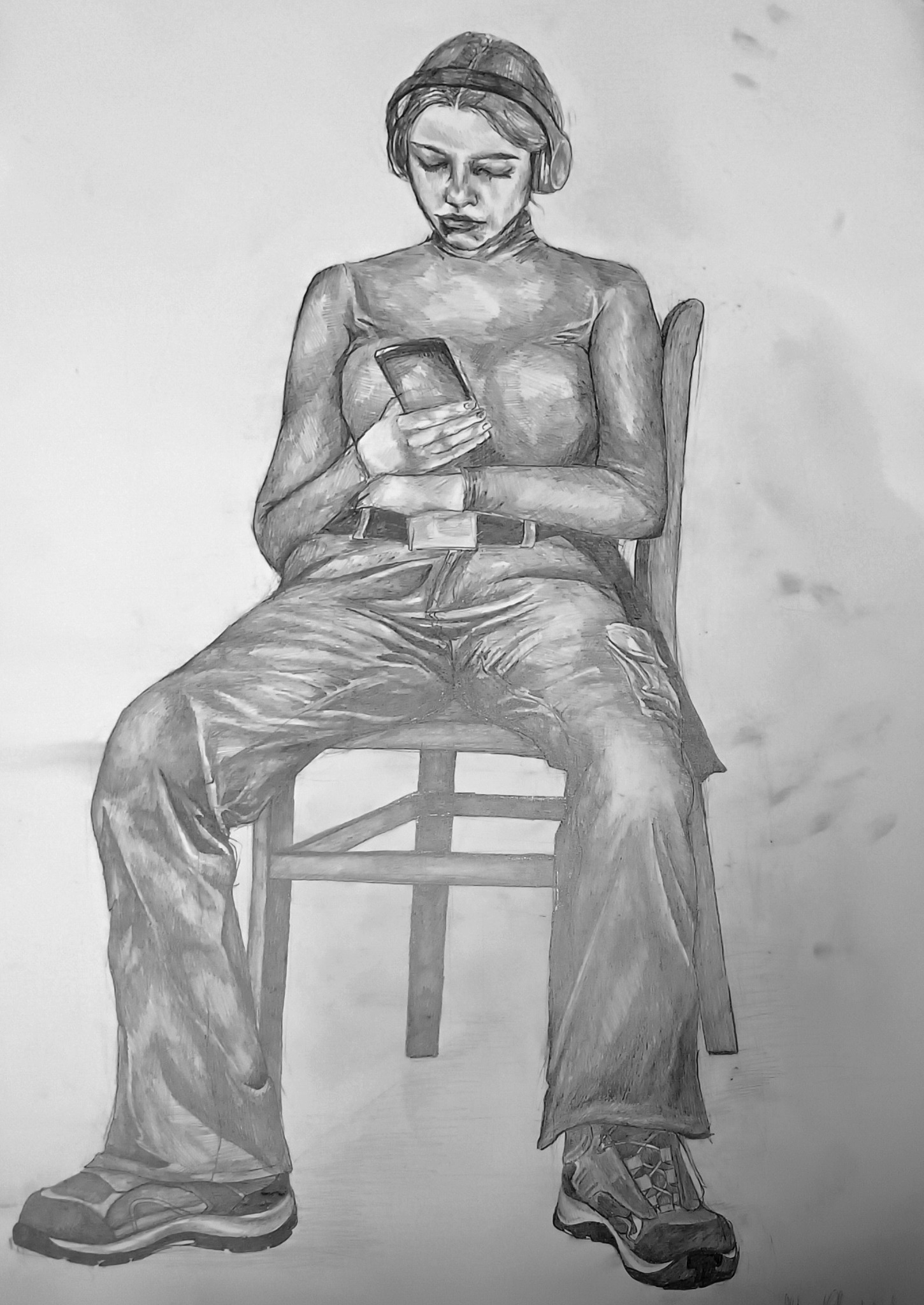Czarno-biały rysunek ołówkiem przedstawiający siedzącą kobietę w słuchawkach, spoglądającą na telefon komórkowy, ubrana w golf, spodnie i buty trekkingowe, siedząca na drewnianym krześle na jasnym...