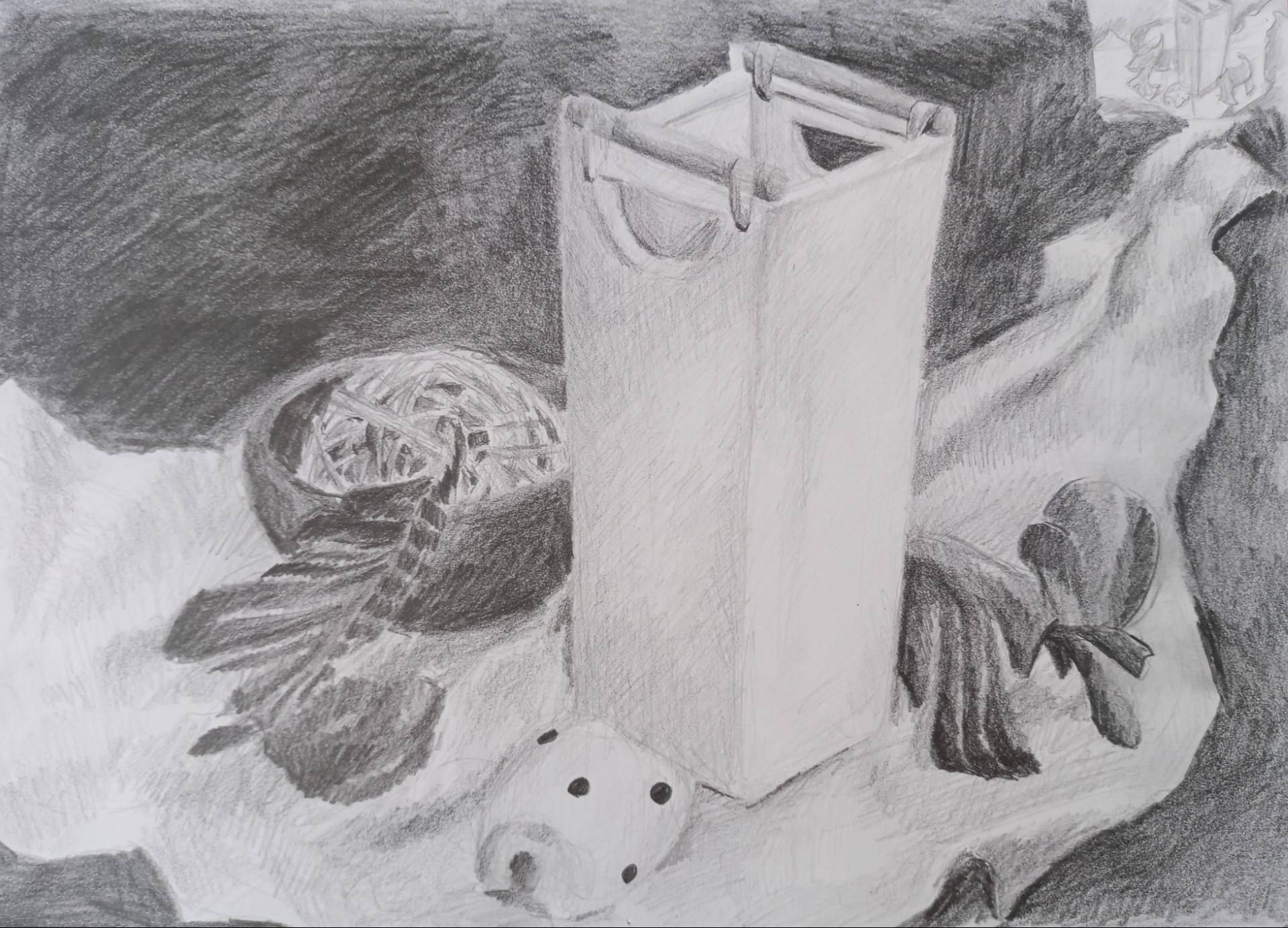 Szkic ołówkiem przedstawiający martwą naturę z pudełkiem, kulą, kostką do gry i draperią, wykonany z widocznymi pociągnięciami ołówka.