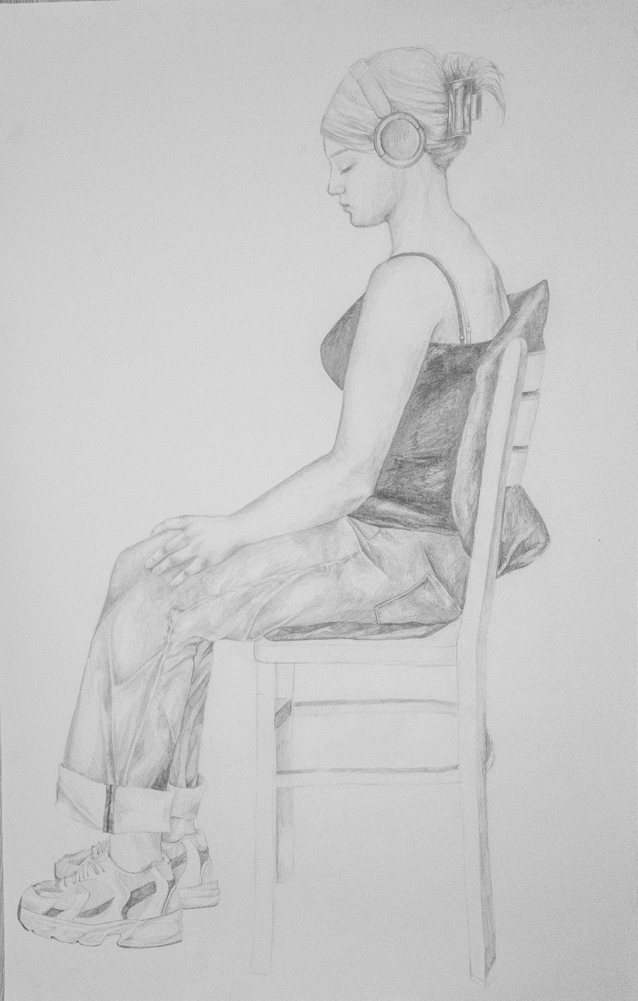 Szkic ołówkiem: siedząca kobieta w słuchawkach, z profilu. Widoczne detale ubioru i krzesła. Stonowana kolorystyka, delikatne cieniowanie.