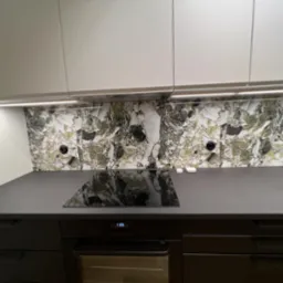 Nowoczesna kuchnia z czarnymi szafkami i blatem, marmurowym panelem nad blatem oraz oświetleniem LED pod szafkami wiszącymi.