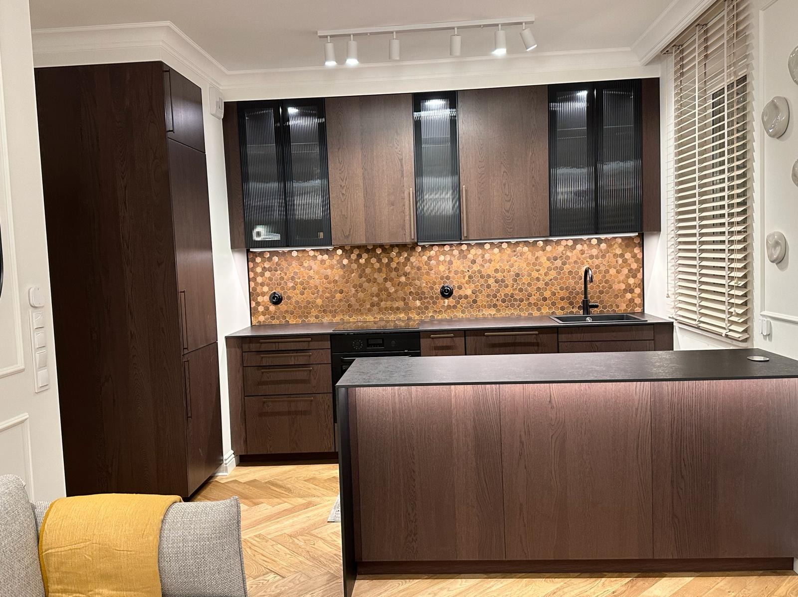 Nowoczesna kuchnia z ciemnego drewna z wyspą, heksagonalnymi płytkami na ścianie i oświetleniem punktowym