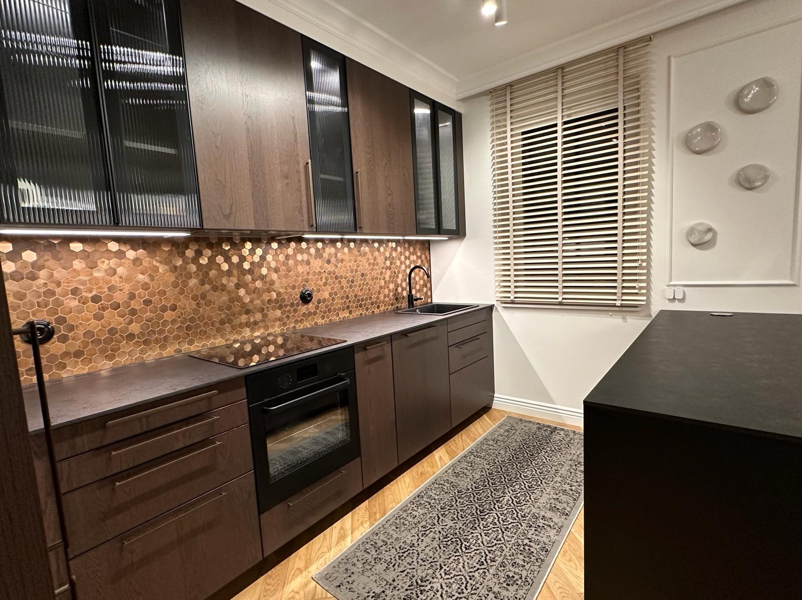 Nowoczesna kuchnia z brązowymi szafkami, heksagonalną mozaiką na ścianie, czarną armaturą i drewnianymi żaluzjami.