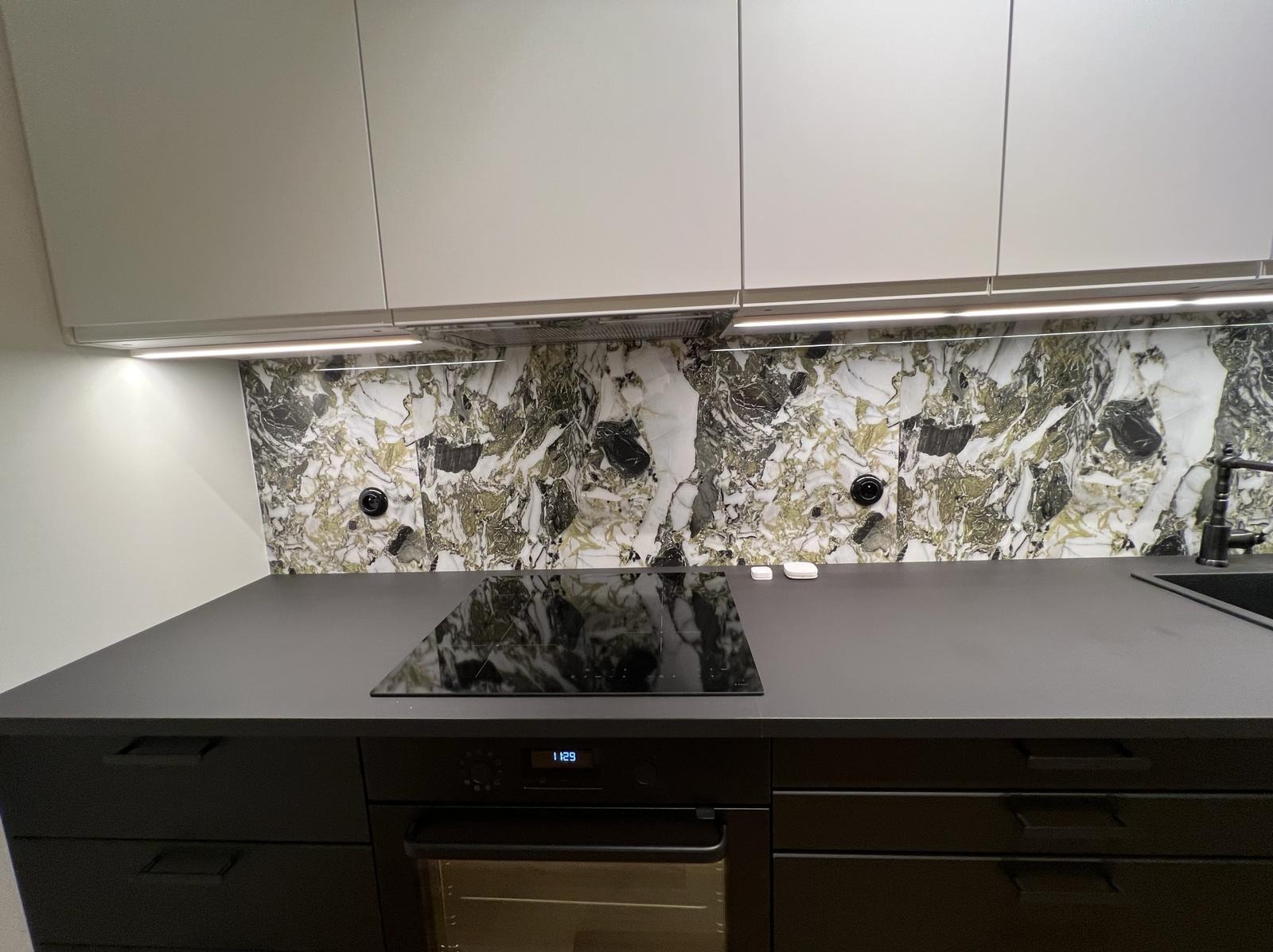 Nowoczesna kuchnia z czarnymi szafkami i blatem, marmurowym panelem nad blatem oraz oświetleniem LED pod szafkami wiszącymi.