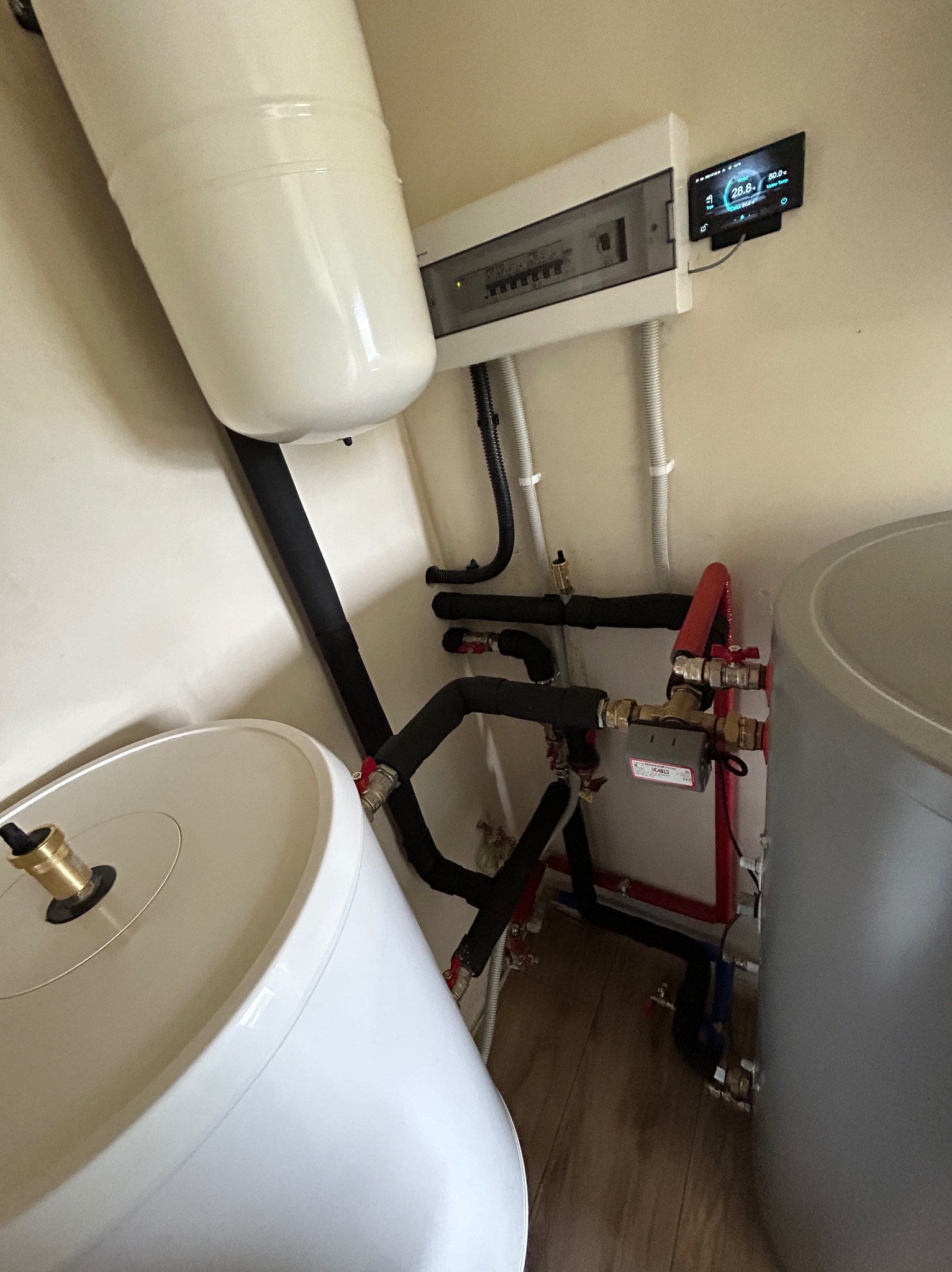 Instalacja dwóch zbiorników z czarnymi rurami izolacyjnymi i czerwonymi rurami miedzianymi, widoczna tablica rozdzielcza i panel sterowania w Legnicy.